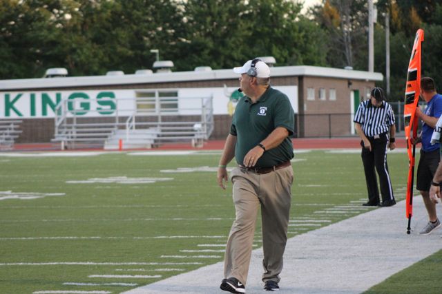 A coach in green watches from the sideline.