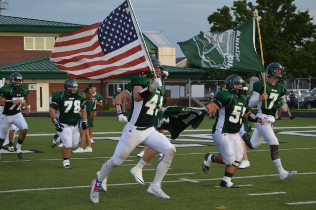 Whiting players run onto the field carrying American and team flags.