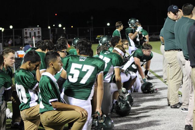 A coach speaks to players seated along the sideline.