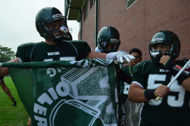 Whiting players prepare a green team flag beside a brick wall.