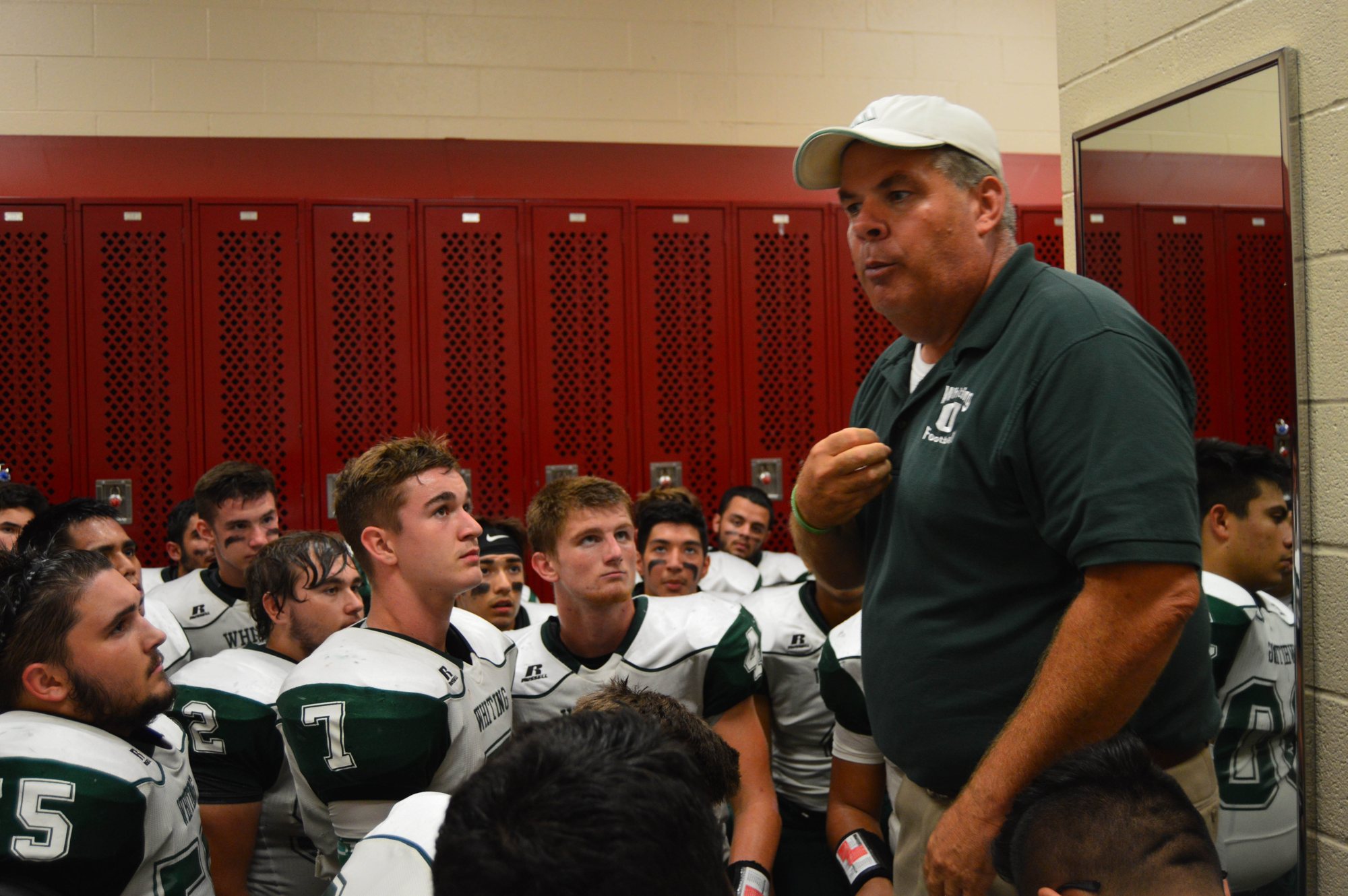 A coach addresses attentive players in front of red lockers.
