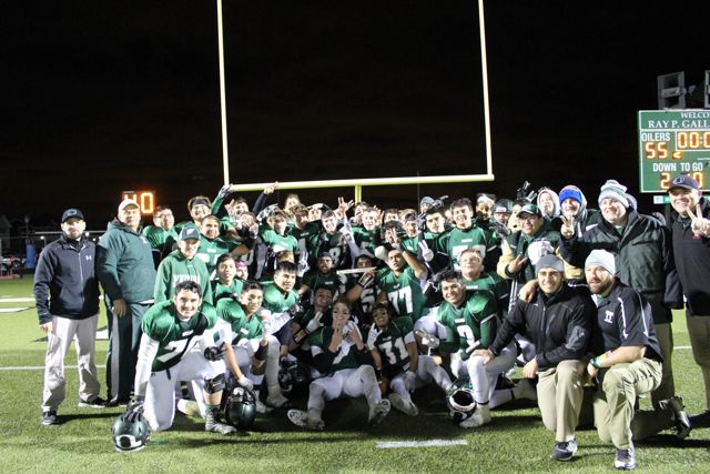 Players, coaches and supporters pose with a trophy beneath the goalposts.
