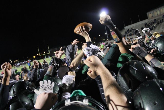 Players raise a football above a tightly gathered group of helmets.