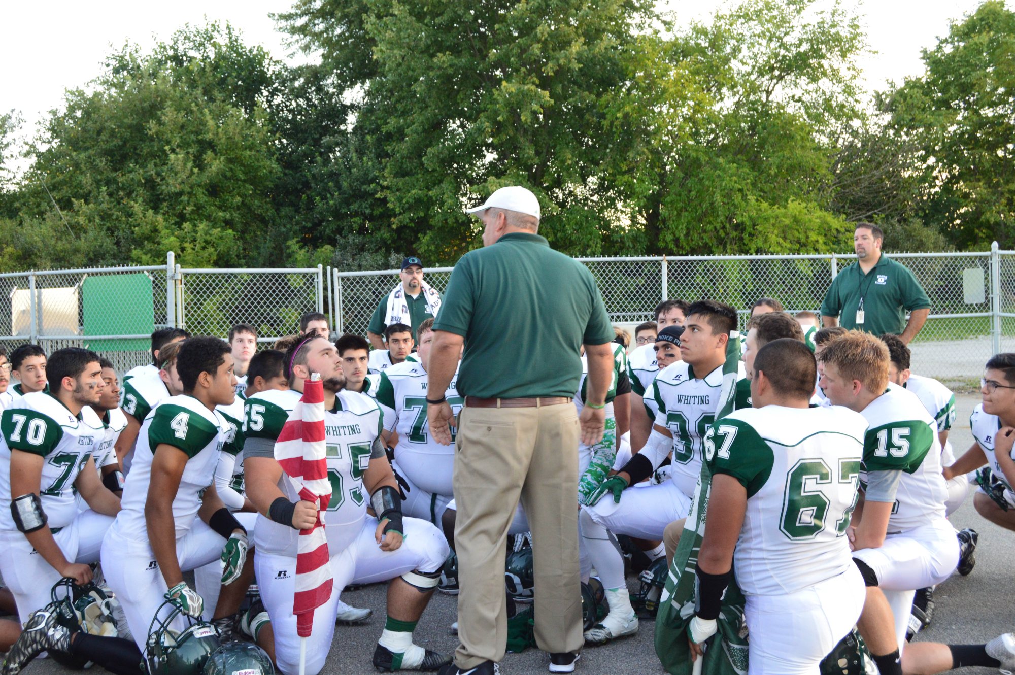 A coach addresses kneeling players in a daylight team huddle.