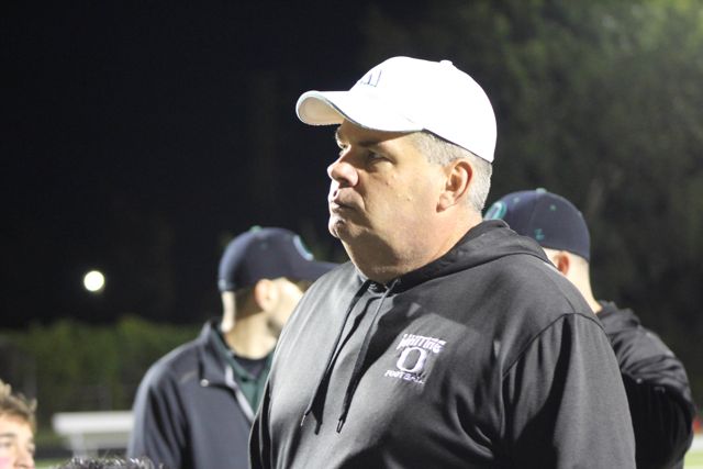 A coach in a white cap watches from the field.