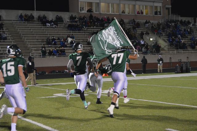 Whiting players carry a green team flag onto the field.