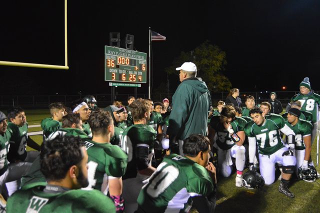 A coach addresses kneeling players beneath the scoreboard.